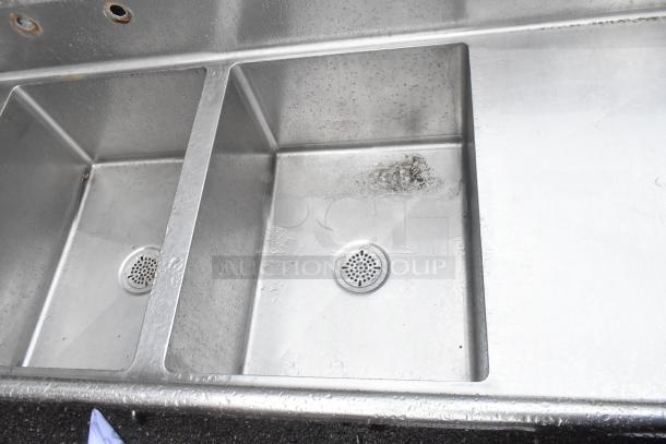 Stainless steel 3-bay sink with dual drain boards, showing signs of wear; no legs included. Visible drain covers.