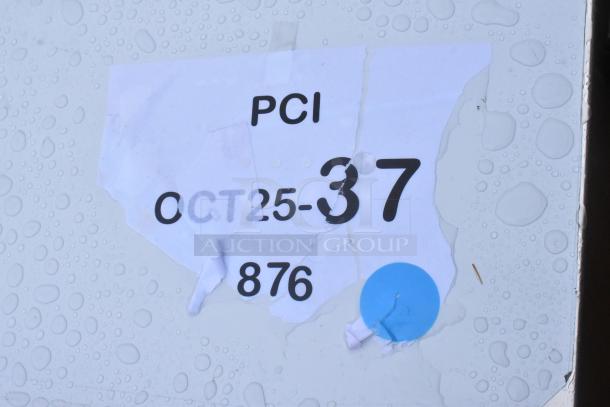 Damaged paper label with "PCI" and "OCT25-37" marked on a surface with water droplets.