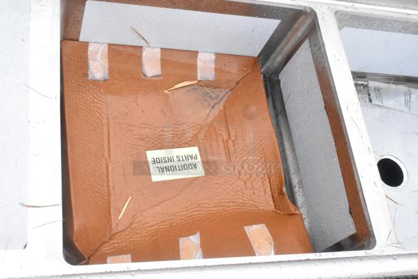 BRAND NEW Regency 600S22323224 two-compartment stainless steel sink with scratches and dents, includes two drainboards and galvanized steel legs. Brown cardboard inside marked "Additional Parts Inside."