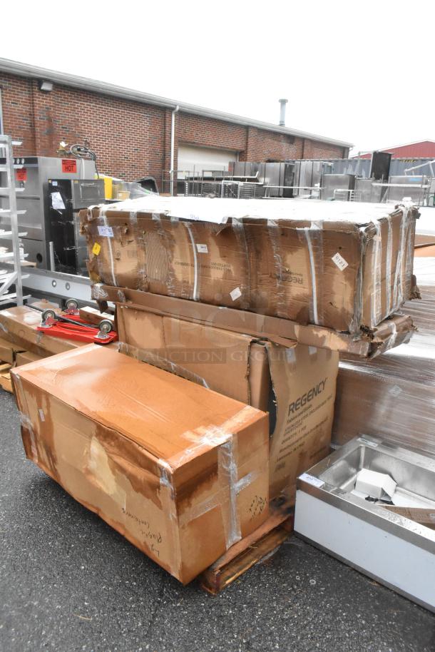 Boxes containing 4 new stainless steel items by Regency, including a pass-through shelf and enclosed base table. Labels visible.