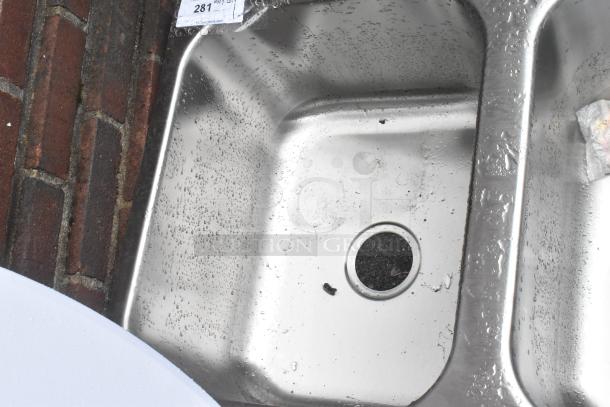 Brand new stainless steel 3 bay drop-in sink with visible scratches and dents, water droplets, and auction tag #281.