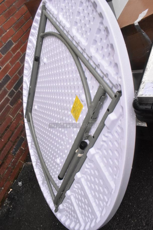Brand new, white round folding table with scratch and dent. Features sturdy metal legs, textured surface, and caution label.