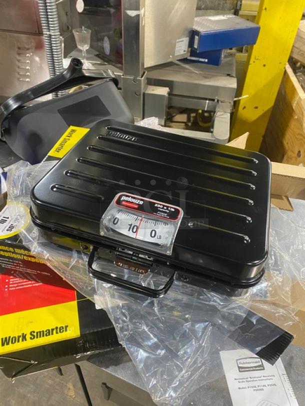 Brand new Rubbermaid Pelouze FGP250S 250 lb. mechanical shipping scale in black briefcase-style, on legs, with visible label.