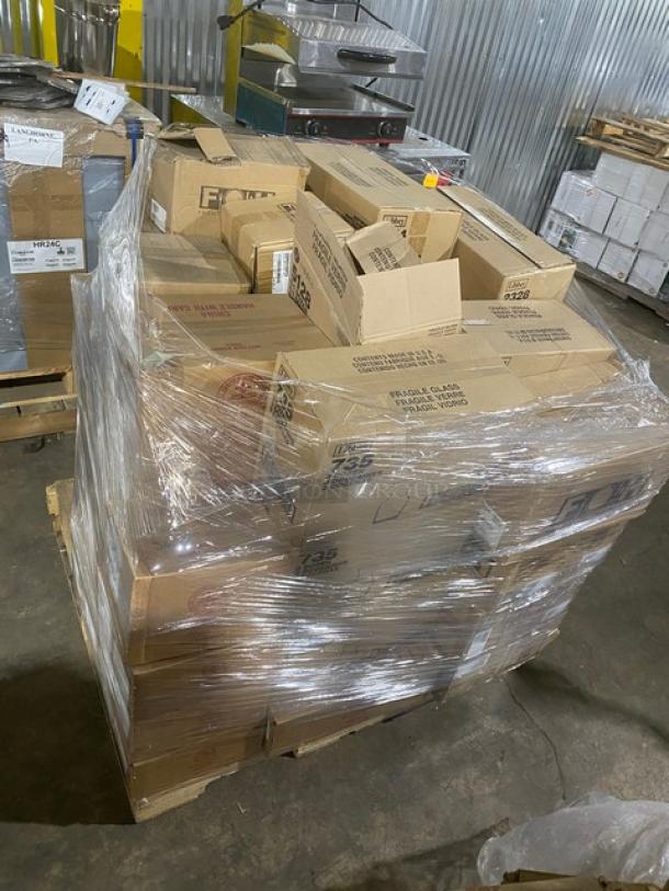 Stacked pallet of mixed boxes, wrapped in plastic, containing new commercial porcelain dishes and glassware.