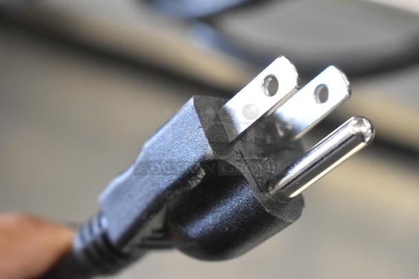 Close-up of a power plug for the 2025 Mahlkonig E65W GBS espresso grinder, showing metal prongs and black plastic casing.
