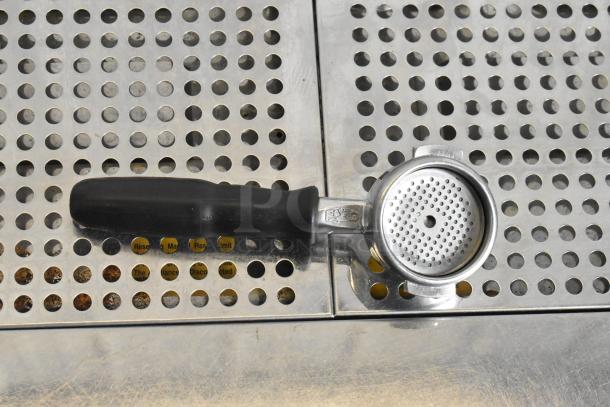 La Marzocco espresso machine portafilter on perforated stainless steel drip tray, black handle visible.