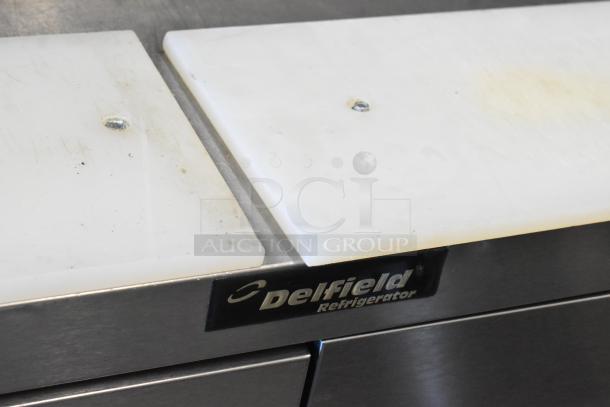 Delfield stainless steel prep table with cutting boards, four drawers, and over-shelf. Visible wear.