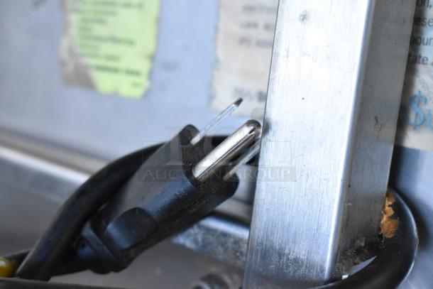Delfield stainless steel prep table plug and metal surface close-up, showing part of attached cords.