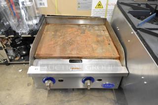 Globe stainless steel countertop gas griddle, rusted surface, dual control knobs, warning label visible, model unspecified.
