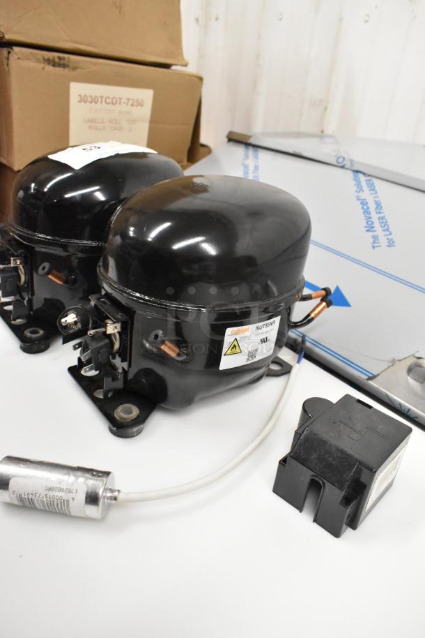 Two brand new Cubigel compressors, models NUT55NR and NUT70NR, 115-127 volts, 1 phase, shown with attached components.