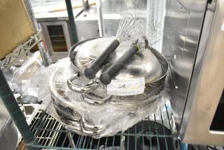 Nine brand new scratch and dent metal pots with lids and whisks, wrapped in plastic, auction label visible.
