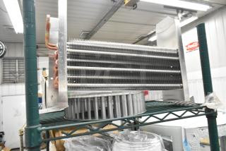 Brand new scratch and dent evaporator coil and blower piece on shelf, showcasing metal fins and copper tubing.