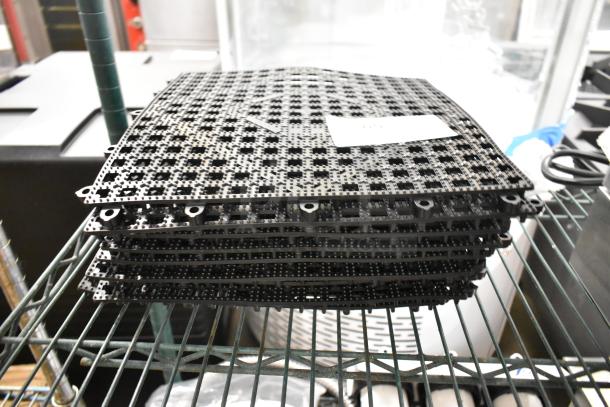 10 brand new black floor mat pieces, scratch and dent condition, stacked on a metal shelf.