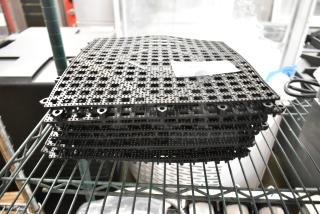 10 brand new black floor mat pieces, scratch and dent condition, stacked on a metal shelf.