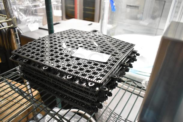 10 brand new black floor mat pieces, rugged texture, minor scratches, stacked on a shelf. Paper tag visible.