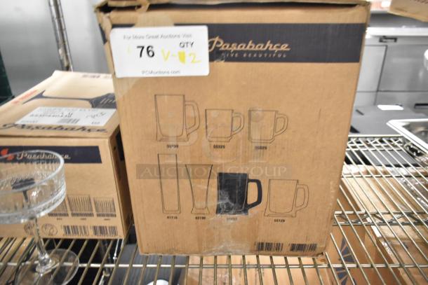 Pasabahce Elysia 9 oz. coupe glass and 22 oz. beer mug from Steelite International in unopened boxes on a metal shelf.