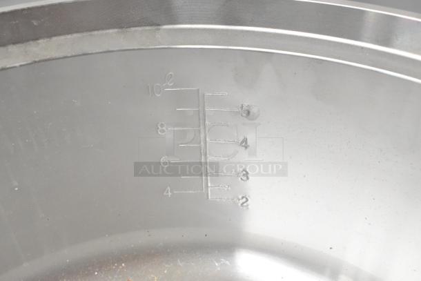Stainless steel surface with volume markings, showing up to 10 liters. Surface appears clean with minor scratches.