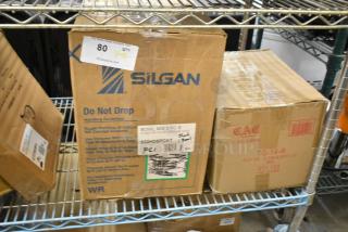 Two boxes on a metal shelf. One labeled 922HD8PCKT, contains Vollrath 8-piece stainless mixing bowls. Another, CAC TG-14-R, holds red oval platters. Both brand new.