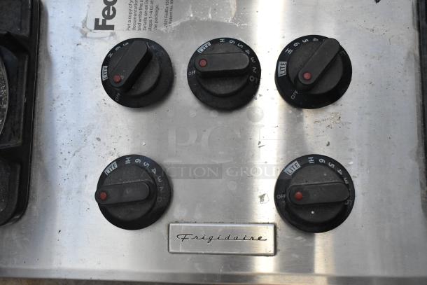 Frigidaire PLGC36S9CCB gas range control knobs, showing five black dials on a metallic surface with visible wear.
