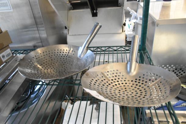 Three brand new metal skimmers with perforations, slight scratches and dents, on a shelf. Durable kitchen utensils.