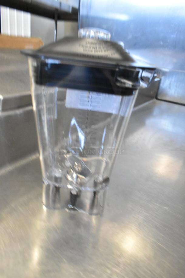 Brand new clear poly blender pitcher with minor scratches and dents. Features measurement markings and a black lid.