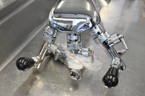 Chrome-plated control valves with "Sparkling," "Room," and "Cold" labels, wrapped in protective plastic, on a metal surface.