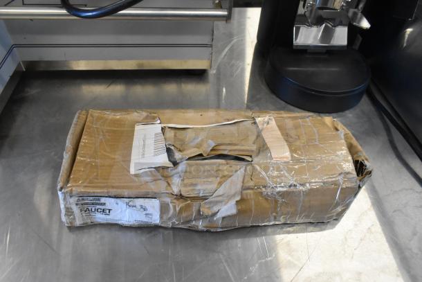 Damaged cardboard box labeled "Assure Faucet" on a metal surface, indicating new items inside despite package condition.