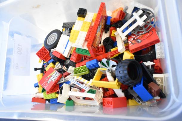 Box of assorted Lego pieces in various colors and shapes, including wheels and printed blocks, in used condition.