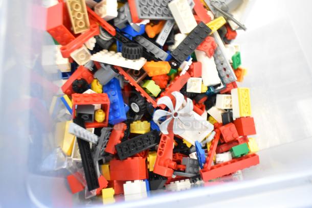 Box of assorted Lego pieces in various colors and shapes, including bricks, wheels, and propellers.