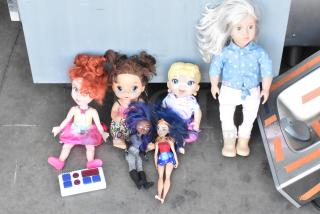 Lot of assorted dolls, varying styles and sizes, laid on a floor. Includes a bright-haired doll and accessories. Items show moderate wear.
