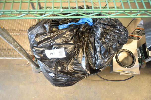 Lot of various items in a black bag labeled "197 QTY," including dolls, on a metal shelf. Items condition unknown.