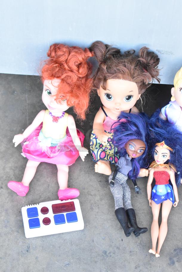 Lot of various dolls, including one with red curly hair and pink dress, others in diverse outfits. Includes a remote control.