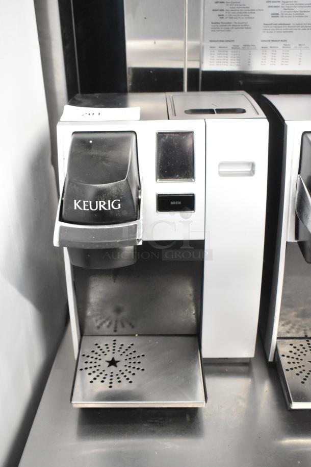 Two Keurig K150 coffee makers, countertop models, slightly used. Features include single cup brewing and LCD screen.