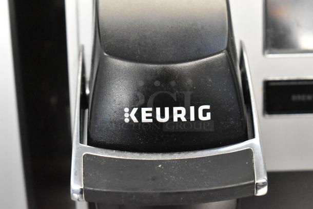 Keurig K150 countertop single cup coffee maker in black, close-up of logo and spout, modern design, excellent condition.