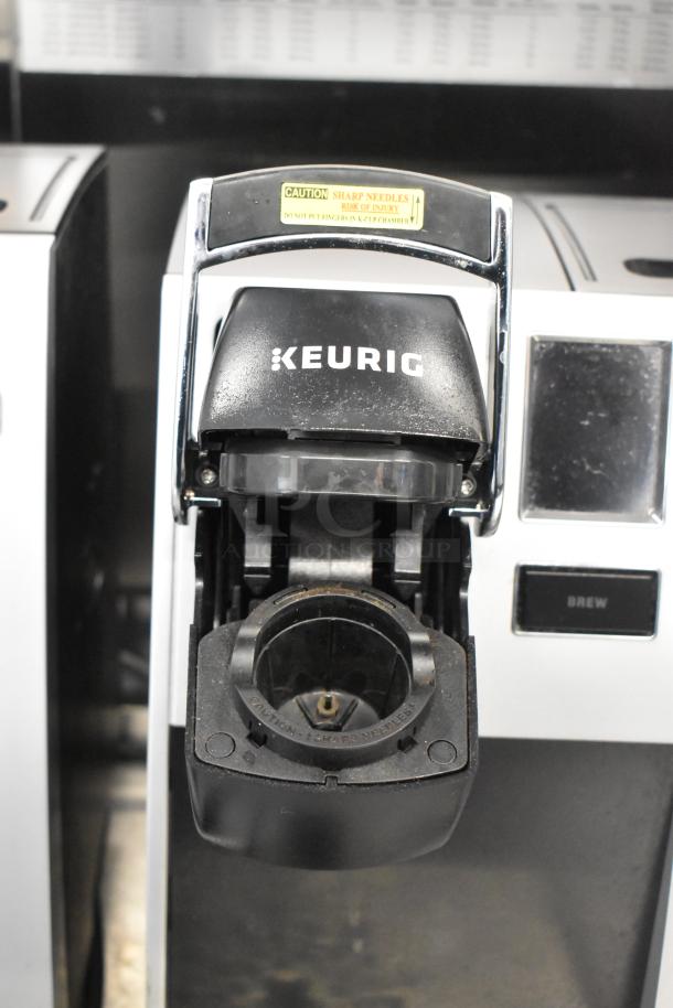 Keurig K150 single cup coffee maker with open brew chamber. Visible safety caution for sharp needles. Good condition.