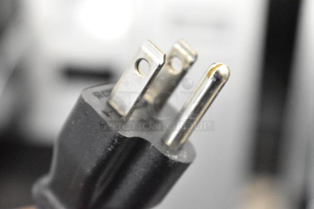 Close-up of a three-prong plug for a Keurig coffee maker, indicating the device's electrical connection.