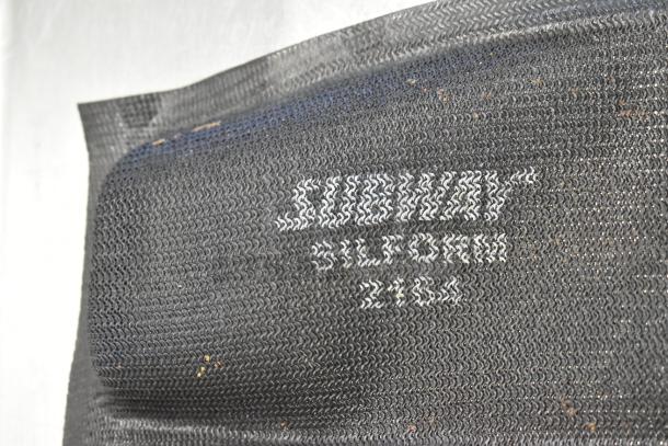 Close-up of a black baking pan liner with visible white text reading "SILFORM 2463". Textured surface with minor debris.