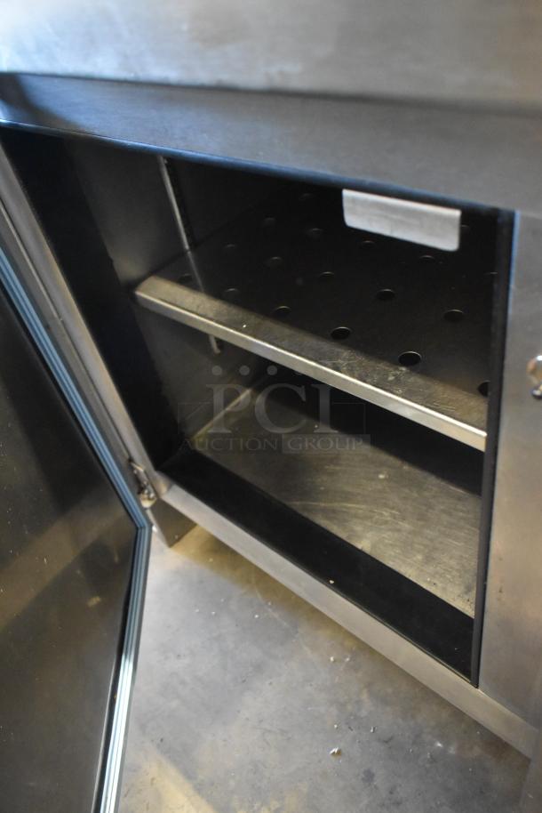 Stainless steel commercial pizza prep table with open door showing interior shelves. Equipped with commercial casters, 115 volts, 1 phase.