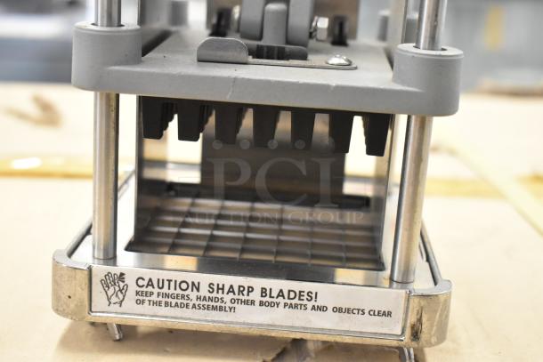 Metal countertop vegetable cutter with sharp blades, sturdy frame. Caution label advises safety around blade assembly.