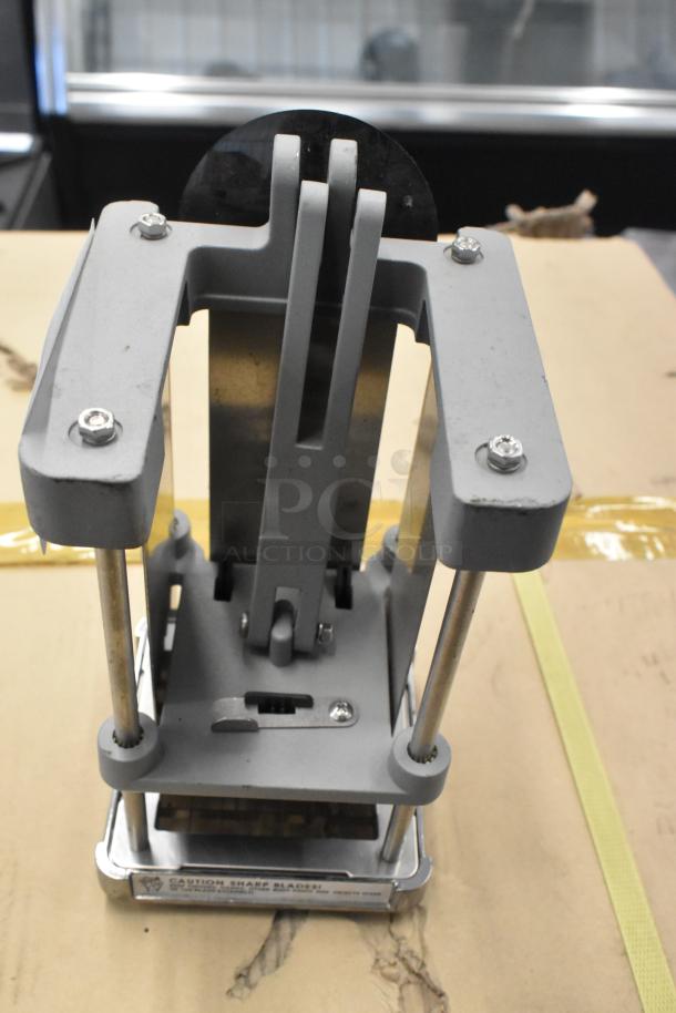 Metal countertop vegetable cutter with sturdy frame and sharp blades. Slight wear on the surface, labeled for safety.