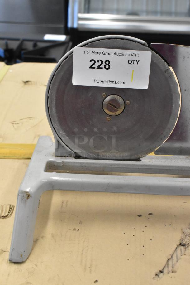 Metal countertop manual meat slicer with a circular blade. Item tag reads "228", indicating auction details. Slight wear visible.