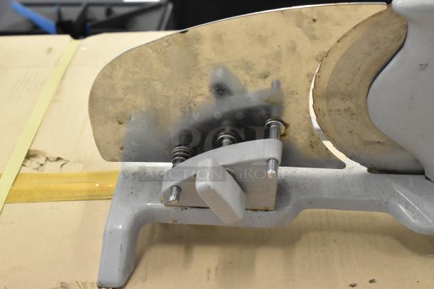 Metal countertop manual meat slicer with stainless steel blade. Features sturdy base and adjustable handle, visible wear.