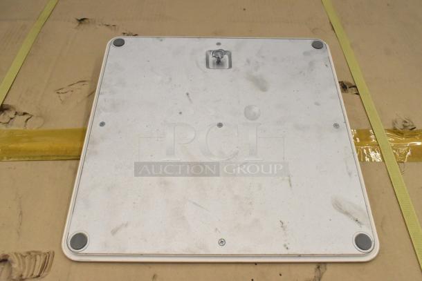 A slightly worn, rectangular metal panel with rounded corners, screws, and rubber feet on cardboard.