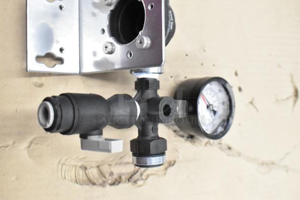 Assorted mechanical parts including a pressure gauge and metal fittings, set on cardboard.