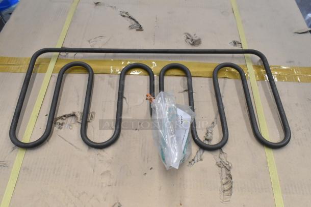Metal burner with sinuous heating elements, new condition. Includes labeled bag with parts, placed on a cardboard surface.
