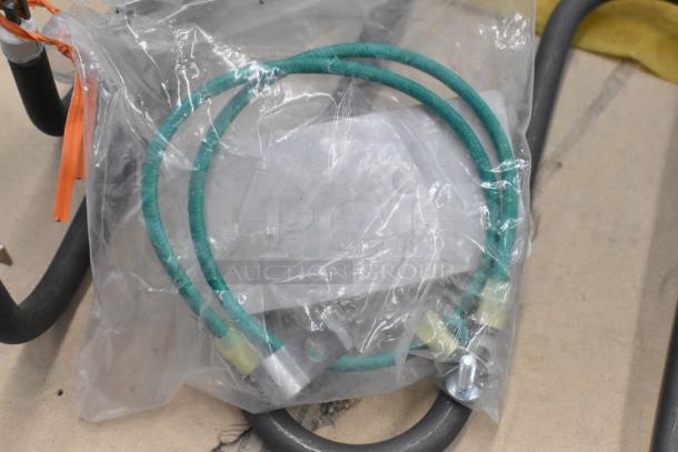 Sealed metal burner with green hose and mounting hardware inside plastic packaging, appears new.