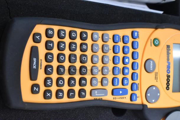 Dymo RhinoPro 5000 label printer, orange and black design, in protective hard case. Features QWERTY keys, function buttons.