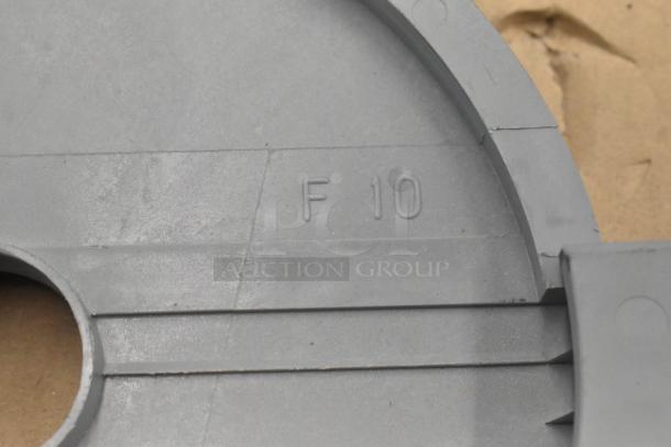 Close-up of a food processor blade marked "F 10" on a grey surface, part of a set including an S-blade and slicing blade.