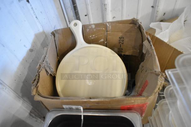 Cardboard box with various items including a white skillet and black bus bins. Box is open and shows some wear.