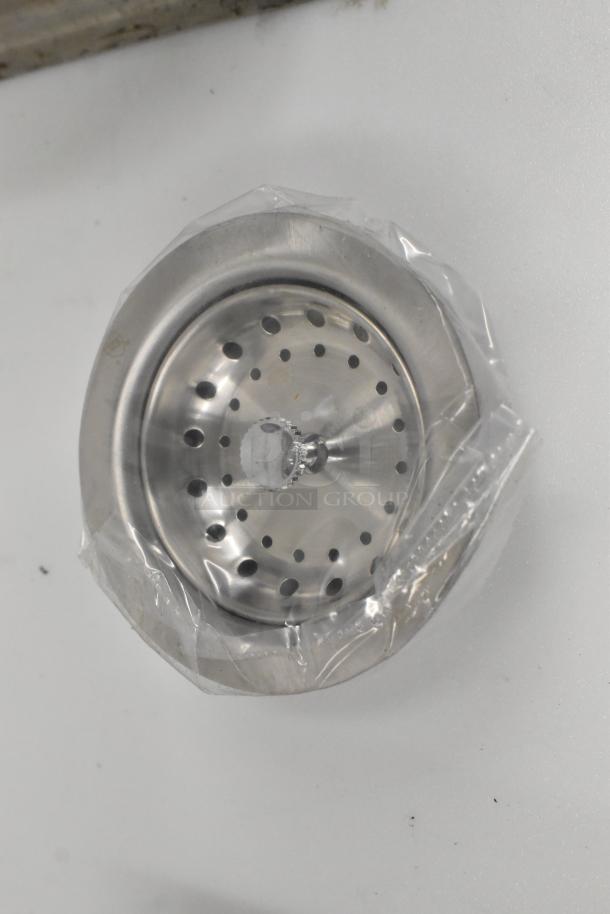 Stainless steel wall mount sink drain, new with scratches and dents, missing one bracket, shown in protective wrapping.